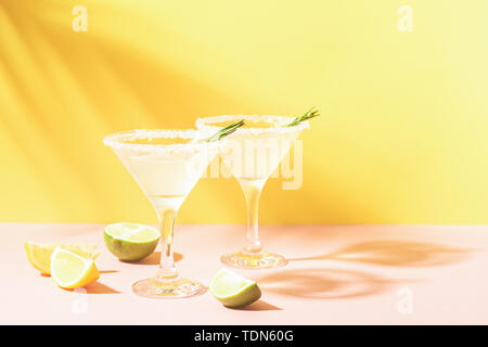 Ein Getränk von Zitrone und Limette im eleganten Brille pastellfarbenen Hintergrund mit strahlendem Sonnenschein. Sommer Limonade oder Mojito. Stockfoto