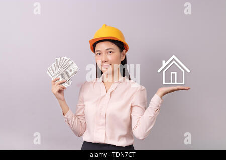 Kredite für Immobilien Konzept, Frau mit gelben Helm Holding banknote Geld in die Hand und weiss Logo home Symbol in der anderen Hand Stockfoto