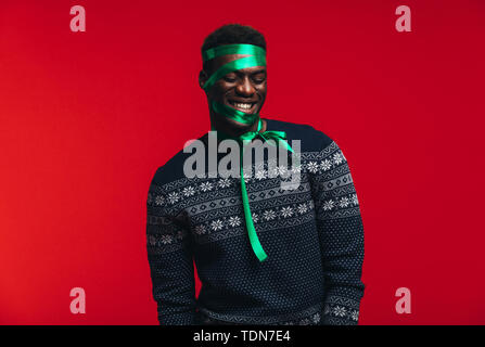 Happy afrikanischer Mann mit Satinband auf seinem Gesicht gegen den roten Hintergrund gebunden. Man verpackt als Geschenk. Stockfoto