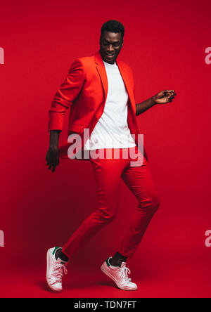 Volle Länge od hübscher junger afrikanischer Mann tanzen auf roten Hintergrund. Mann im eleganten roten Outfit zeigen einige Tanzschritte. Stockfoto