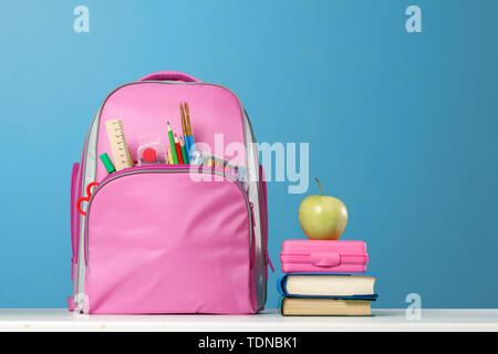 Schüler eingestellt. Rosa Rucksack mit Briefpapier, einen Stapel Bücher, ein Lunchpaket, ein Apfel auf dem Tisch auf einem blauen Hintergrund. Zurück zu Schule. Stockfoto