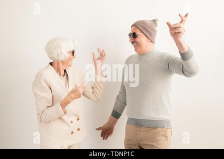 Gerne älteres Paar in Sonnenbrille und casualwear Freizeit genießen beim Tanzen auf weißem Hintergrund im Studio Stockfoto