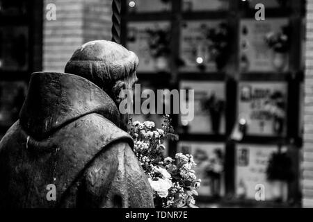 Hintere Statue von einem Mönch mit einem Strauß Blumen auf dem Friedhof von Parma. In der Ferne sind die grabsteine von den Gräbern. Stockfoto