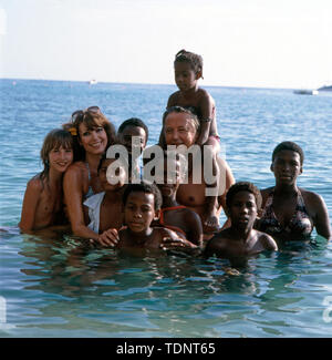 Die deutsche Fernsehmoderatorin, Programmsprecherin, Plant und ehemalige Miss World Petra Schürmann posiert mit Ihrem Partner Gerhard Freund und Tochter Alexandra Freund sowie einheimischen Kindern im Meer, Ca. 1978. Die deutsche TV-Moderatorin, Programm Ansager, Schauspielerin und ehemalige Miss World Petra Schürmann stellt mit ihrem Partner Gerhard Freund und Tochter Alexandra Freund sowie lokale Kinder im Meer, ca. 1978. Stockfoto