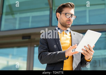 Ernsthafte Kerl in formale Surfen auf Websites und bei Anzeige der digitalen Tablet in städtische Umwelt Stockfoto