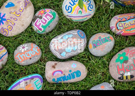 Kinder Hand gemalte Wörter auf Kieselsteinen auf einem Garten psychische Gesundheit Therapie Anzeige an eine Blume zeigen. Großbritannien Stockfoto