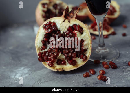 Bei einem Glas Wein auf einem grauen Hintergrund unter Granatäpfel. Schließen Granatapfel Granatapfel und roten Samen. Das Bein von einem Glas Becher neben dem Obst. Stockfoto