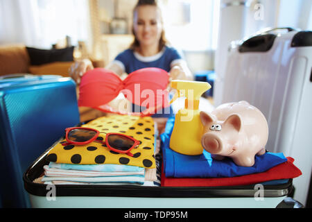 Nahaufnahme auf gerne stilvolle Frau in Blau t-shirt mit piggy Bank berechnet Sommer Budget bei modernen Haus im sonnigen Sommertag. Stockfoto