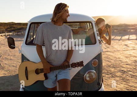 Mann mit Gitarre an Frau mit digitaler Kamera schaut aus dem Fenster des Reisemobils Stockfoto