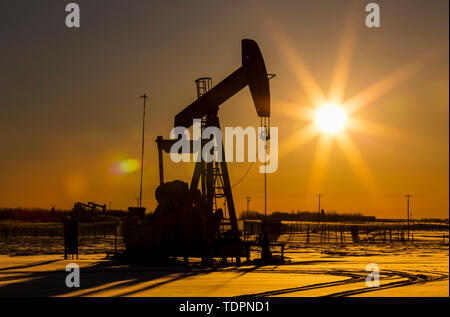 Silhouette von pumpjack im Schnee mit einem orangefarbenen starburst Sun bei Sonnenaufgang; Longview, Alberta, Kanada Stockfoto