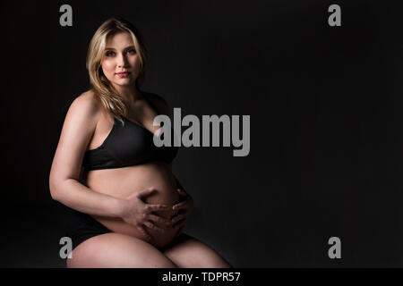 Eine junge schwangere Frau, die Ihre holding Bauch in ein Studio und für die Kamera posieren: Edmonton, Alberta, Kanada Stockfoto