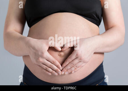 Eine junge schwangere Frau, die Ihre holding Bauch in ein Studio und ein Herz Form über Ihr ungeborenes Kind; Edmonton, Alberta, Kanada Stockfoto