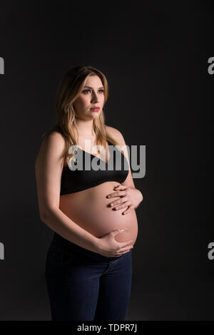 Eine junge schwangere Frau, die Ihre holding Bauch in ein Studio und weg von der Kamera zu Ihrem ungeborenen Kind denken nach: Edmonton, Alberta, Kanada Stockfoto