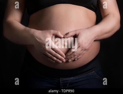 Eine junge schwangere Frau, die Ihre holding Bauch in ein Studio und ein Herz Form über Ihr ungeborenes Kind; Edmonton, Alberta, Kanada Stockfoto