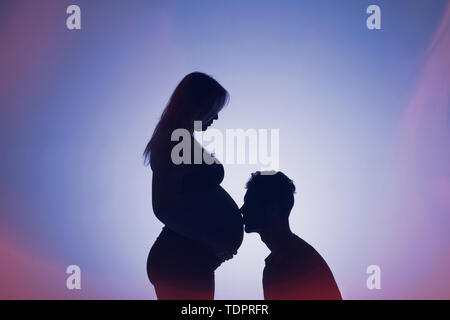 Eine Silhouette in einem Studio der Paare, die ein Baby und der Vater ist Küssen Bauch der Mutter, die ist gut entlang in ihrer Schwangerschaft Stockfoto