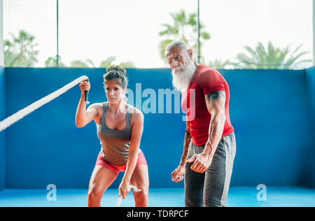 Passende Frau Training mit Schlacht Seil im Fitnessstudio - Hipster personal trainer Motivieren einer weiblichen Athleten wer tut Ausdauerübungen Stockfoto