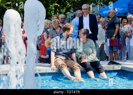 Berlin, Deutschland. Juni, 2019 18. Florian Schmidt (Bündnis 90/Die Grünen), Landrat Friedrichshain-Kreuzberg (l) und Katrin Lompscher (Die Linke), Senatorin für Stadtentwicklung, sitzen an der Quelle und ihre Füße im Wasser halten. Jörg Simon, Vorstandsvorsitzender der Berliner Wasserbetriebe, dahinter steckt in seinem Anzug. Der Brunnen in der Karl-Marx-Allee ist wieder in Betrieb zum ersten Mal nach 27 Jahren der Dürre. Quelle: Annette Riedl/dpa/Alamy leben Nachrichten Stockfoto