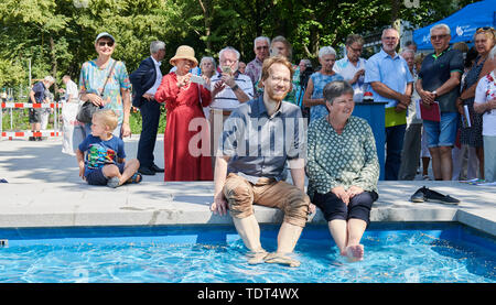 Berlin, Deutschland. Juni, 2019 18. Florian Schmidt (Bündnis 90/Die Grünen), Landrat Friedrichshain-Kreuzberg (l) und Katrin Lompscher (Die Linke), Senatorin für Stadtentwicklung, sitzen an der Quelle und ihre Füße im Wasser halten. Der Brunnen in der Karl-Marx-Allee ist wieder in Betrieb zum ersten Mal nach 27 Jahren der Dürre. Quelle: Annette Riedl/dpa/Alamy leben Nachrichten Stockfoto