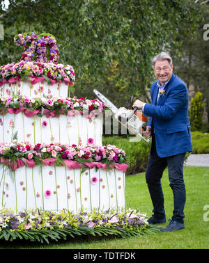 TV Gärtner Alan Titchmarsh vorgibt, riesige dreistufige Blumen Geburtstag Kuchen zu schneiden mit einer Kettensäge bis 70 Jahre der RHS Garden Harlow Carr Mark, während der RHS Garden Harlow Carr Flower Show in Harrogate, North Yorkshire. Stockfoto