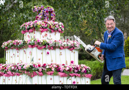 TV Gärtner Alan Titchmarsh vorgibt, riesige dreistufige Blumen Geburtstag Kuchen zu schneiden mit einer Kettensäge bis 70 Jahre der RHS Garden Harlow Carr Mark, während der RHS Garden Harlow Carr Flower Show in Harrogate, North Yorkshire. Stockfoto