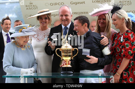 Königin Elizabeth II (links) stellt die Trophäe zu Eigentümer Björn Nielsen (Mitte) und Jockey Frankie Dettori nach dem Gewinn der Gold Cup auf Stradivarius bei Tag drei der Royal Ascot Hotel in Ascot Pferderennbahn. Stockfoto