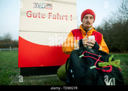 23. November 2018, Sachsen-Anhalt, Halle/Saale: Auf seiner kurzen Reise in die Tschechische Republik, Malte Stolpe eine Auszeit nimmt und isst Brot auf einem Rastplatz an der Autobahn A14 in der Nähe von Halle. Hinter ihm ist das Zeichen für die Autobahn Eingang mit der Aufschrift "Gute Fahrt". Malte ist ein Sport der hitchhiker und Trampte fast 60.000 Kilometer auf seinen zahlreichen Reisen, einschließlich Reisen zum Nordkap. Er beteiligt sich auch an regelmäßigen tramp Rennen und Veranstaltungen. Foto: Johannes Stein/dpa-Zentralbild/ZB Stockfoto