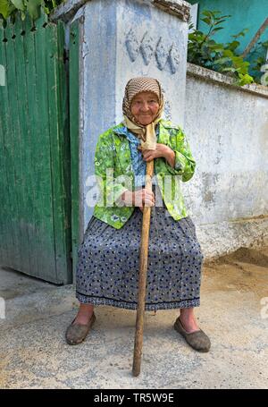 Alte Frau mit Stock vor dem Gartentor, Moldau, Delacau Stockfoto