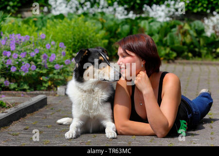 Bearded Collie (Canis lupus f. familiaris), Mischlingen mit weiblichen Besitzer liegen auf Garten weg und bei jedem anderen suchen, Deutschland, Nordrhein-Westfalen Stockfoto