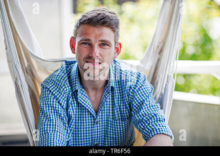 Junge Mann in einem hängenden Sitz sitzt, Deutschland Stockfoto
