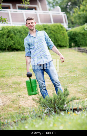 Rosmarin (Rosmarinus officinalis), junge Mann Bewässerung Rosmarin im Garten, Deutschland Stockfoto
