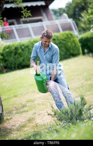Rosmarin (Rosmarinus officinalis), junge Mann Bewässerung Rosmarin im Garten, Deutschland Stockfoto