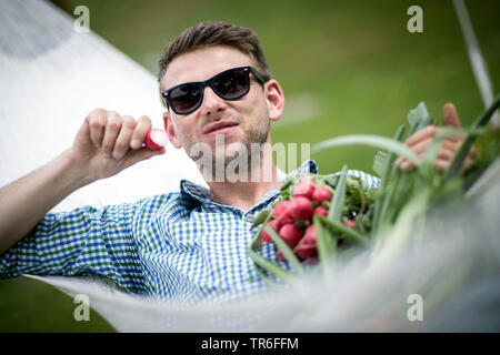 Mann in der Hängematte liegen und Beißen in einem frischen Rettich, Deutschland Stockfoto