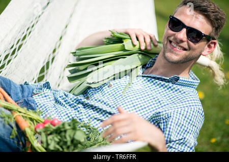 Mann liegen in einer Hängematte mit Lauch, Karotten und Radieschen, Deutschland Stockfoto