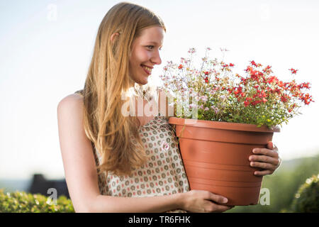 Junge blonde Frau mit einer Topfpflanze in arm, Deutschland Stockfoto