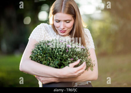 Junge blonde Frau mit einem Aster im Arm, Deutschland Stockfoto