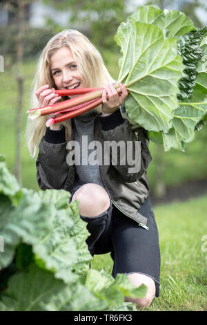 Rhabarber (Rheum rhabarbarum), junge blonde Frau, beißen in frisch gepflückt Rhabarber, Deutschland Stockfoto