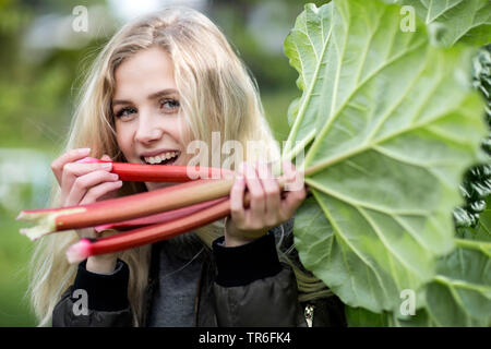 Rhabarber (Rheum rhabarbarum), junge blonde Frau, beißen in frisch gepflückt Rhabarber, Deutschland Stockfoto