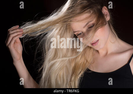 Junge blonde Frau, verloren in Gedanken, ihren Fingern durch ihr Haar, Deutschland Stockfoto