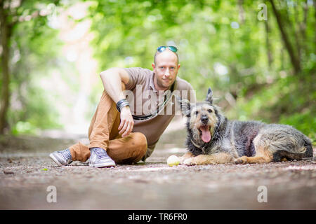 Berger de Picardie, Berger Picard (Canis lupus f. familiaris), Mensch und Hund sitzt auf einem Waldweg, Deutschland Stockfoto
