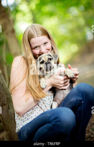 Haushund (Canis lupus f. familiaris), geduckt junge Frau mit einem niedlichen Puggle auf dem Schoß, Deutschland Stockfoto