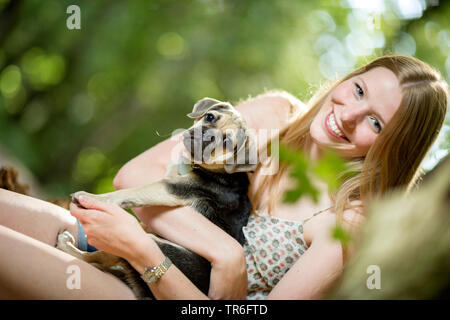 Haushund (Canis lupus f. familiaris), junge Frau mit einem niedlichen Puggle am Arm, Deutschland Stockfoto