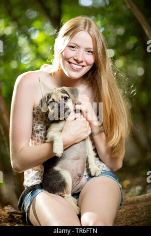Haushund (Canis lupus f. familiaris), junge Frau mit einem niedlichen Puggle auf dem Schoß, Deutschland Stockfoto