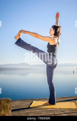 Frau Yoga Übungen an einem See, Utthita Hasta Padangusthasana, Deutschland, Bayern Stockfoto