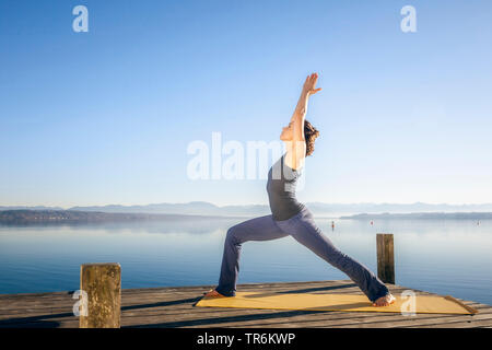 Frau Yoga Übungen an einem See, Virabhadrasana, Deutschland, Bayern Stockfoto