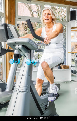 Weibliche senior Sitzen auf einem Fitnessgeräte im Fitness Center, Deutschland Stockfoto