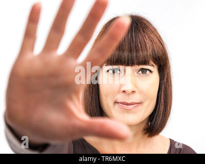 Gut aussehende Frau mit langen braunen Haaren und Fransen Oben Halten einer Hand defensiv, Deutschland Stockfoto