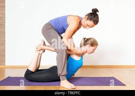 Zwei Frauen Yoga im Wohnzimmer zu Hause tun, mit weiblichen Lehrer helfen fpr Bogen Stockfoto