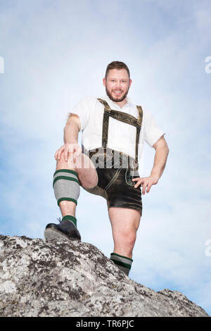 Junger Mann in Bayerische Lederhose auf einem Felsen, Deutschland, Bayern Stockfoto