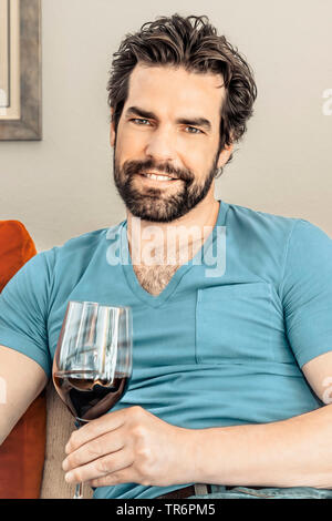 Mann mit Bart auf dem Sofa mit einem Glas Rotwein, Deutschland Stockfoto