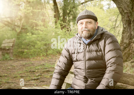 Mann mit Bart und Wooly hat auf einer Bank sitzen in der Natur, Deutschland Stockfoto